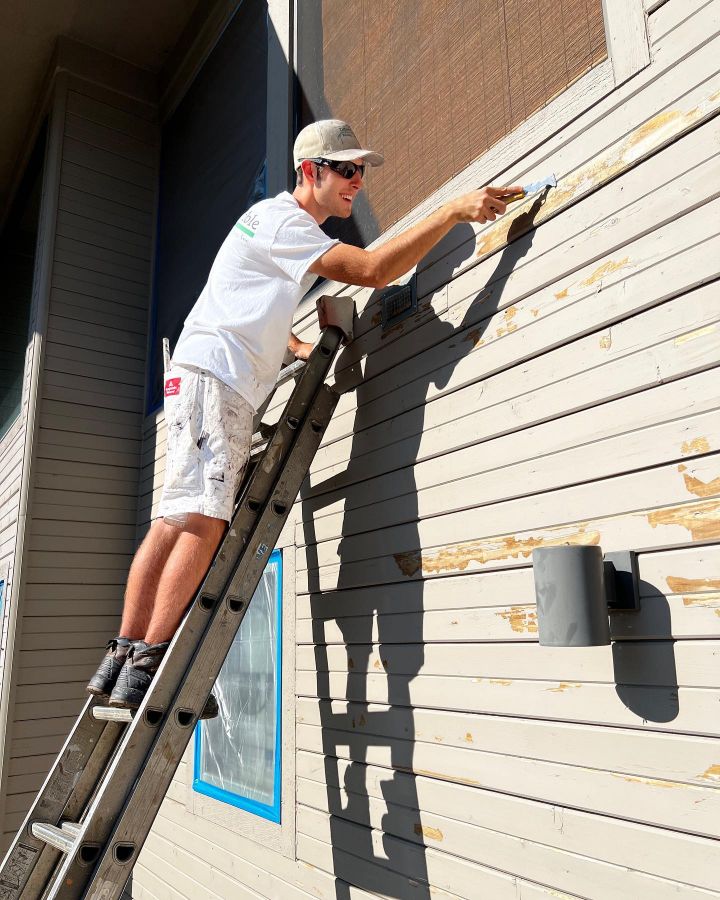 Scraping damaged paint off of a house before painting