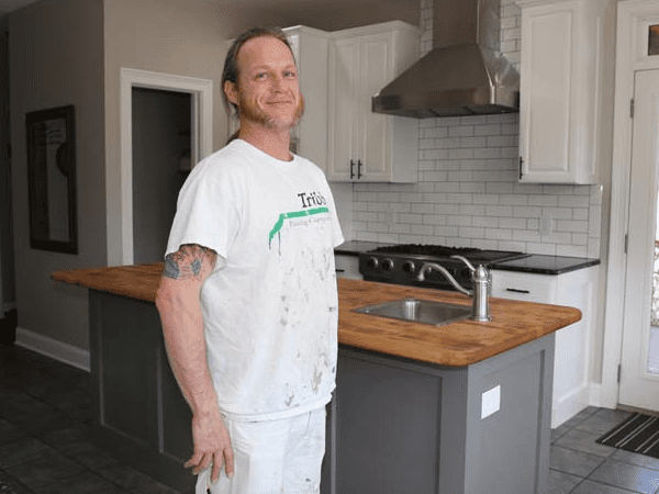 Aaron standing in front of kitchen cabinets he painted