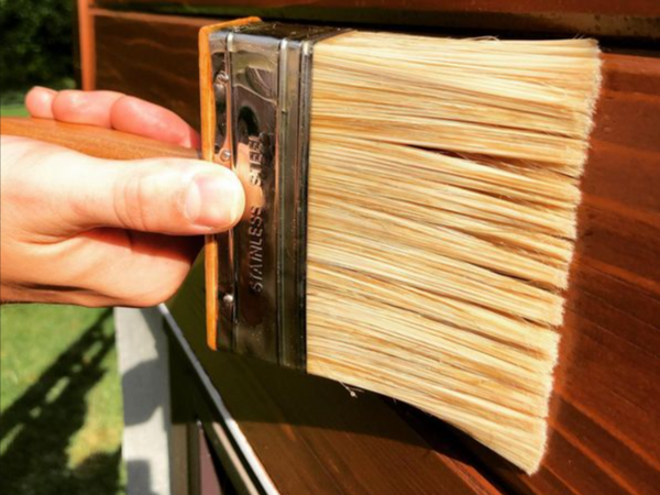 A close up of a hand holding a brush and applying the best exterior stain for wood siding.