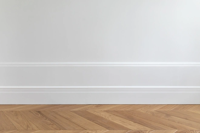 Fragment of classic white interior with wooden french herringbone parquet floor and installed wall panels, decorated with moldings and skirting boards.