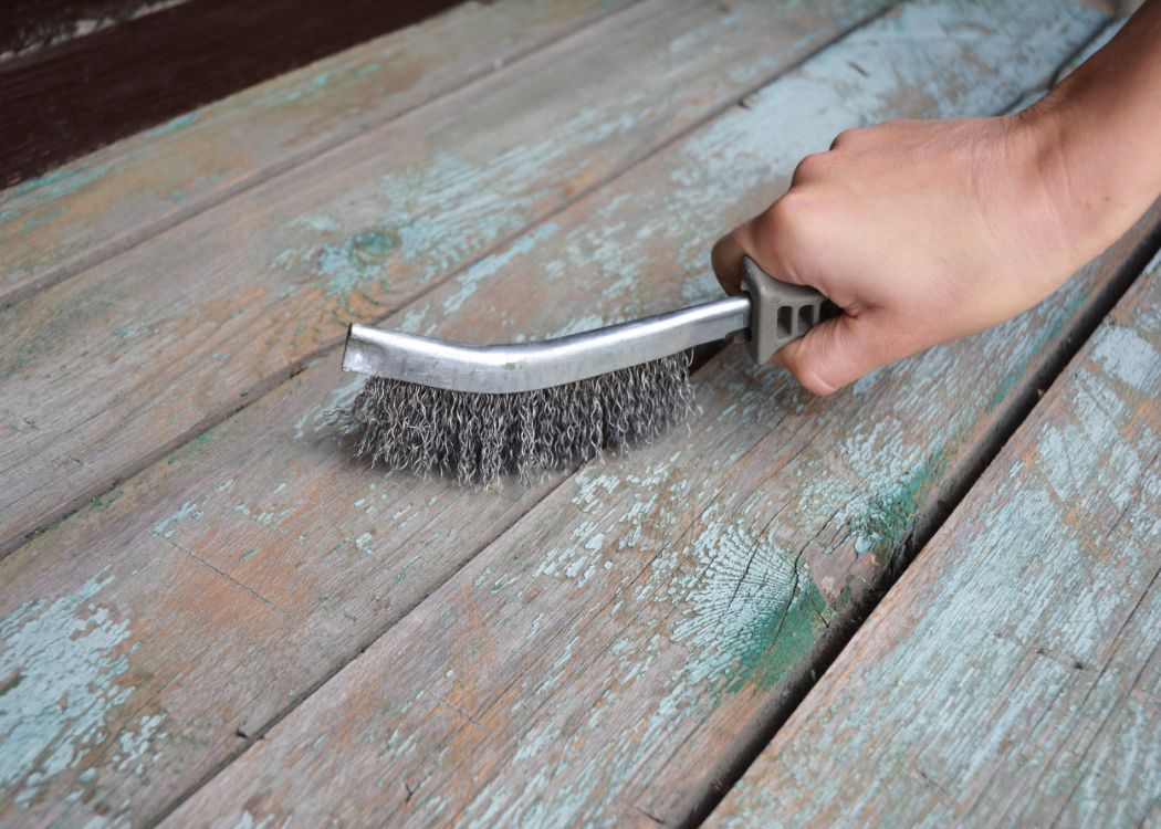 Man remove the old paint from the wooden surface with wire brush