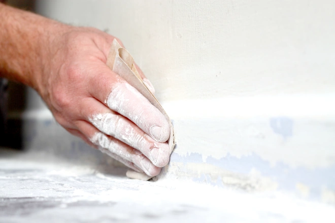 Man sanding base board with sand paper.