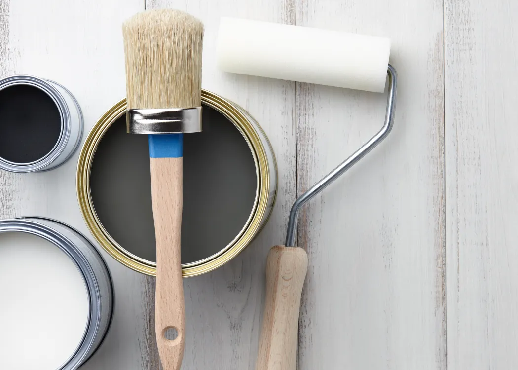 Paint-brush-sponge-roller-paints-waxes-and-other-painting-or-decorating-supplies-on-white-wooden-planks-top-view